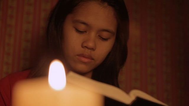 A young girl reads the scriptures by candle light