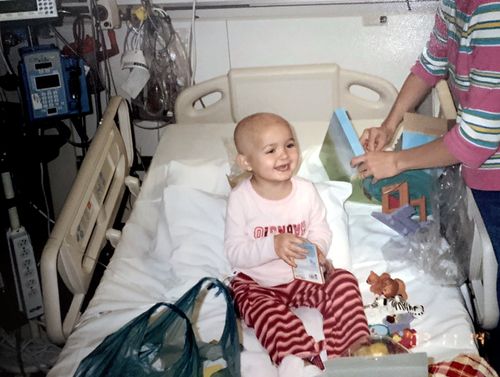 a young girl with leukemia sits in a hospital bed and smiles
