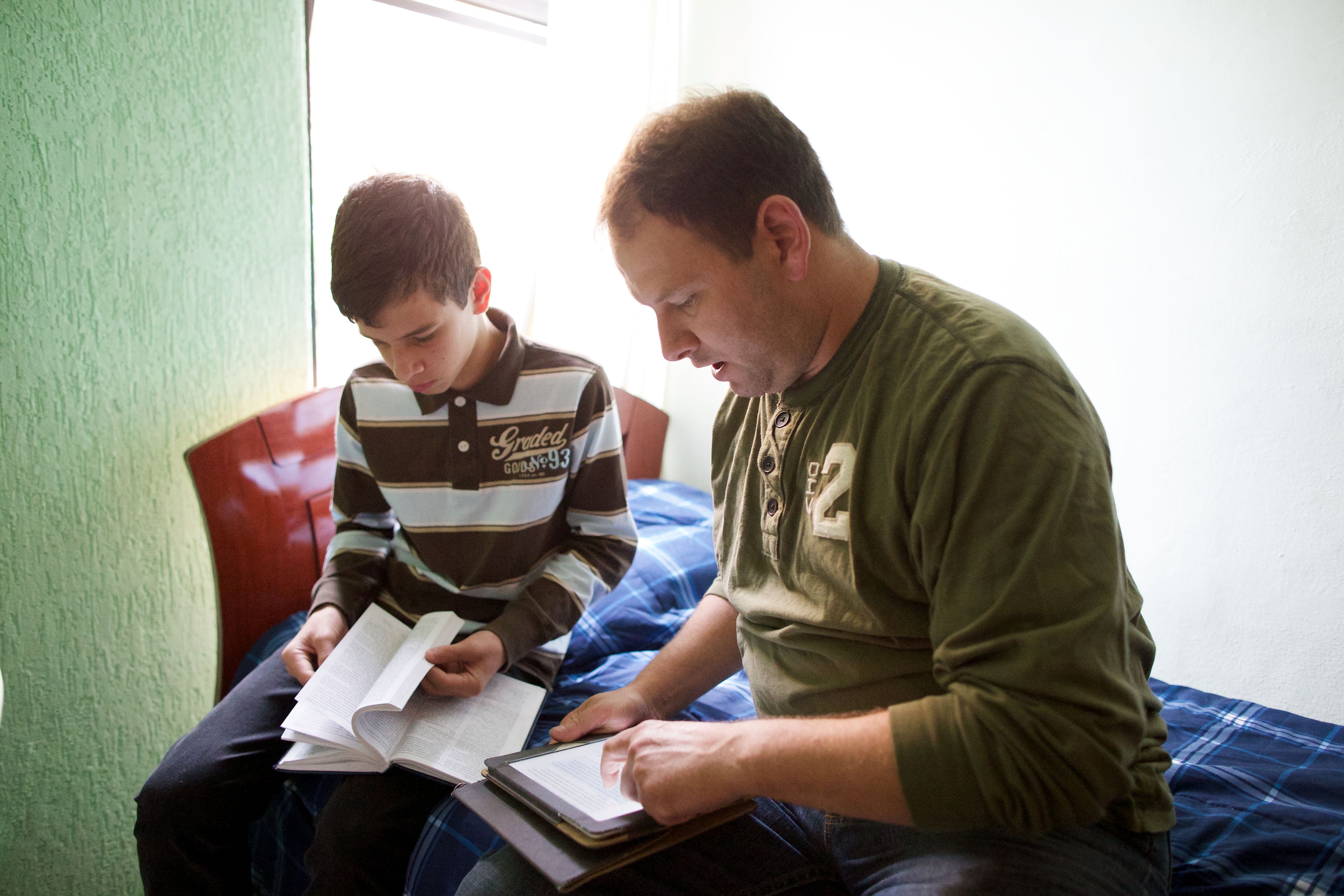 A father and his son sit together and read from the scriptures.
