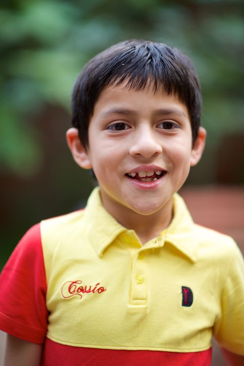 A boy from Peru with short brown hair wearing a yellow and red shirt.