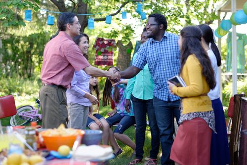 A photo of friends shaking hands at a picnic, with sister missionaries in the foreground. 