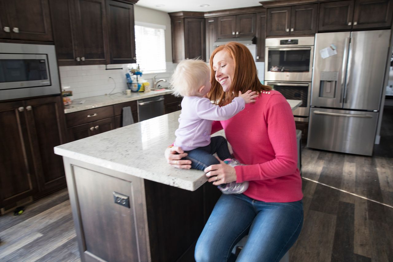 A mother sits with her young child in their kitchen