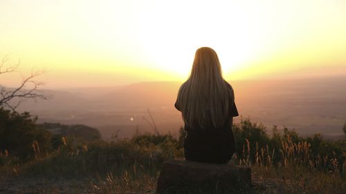 A picture of young woman sitting on the top of a hill reflecting on life.