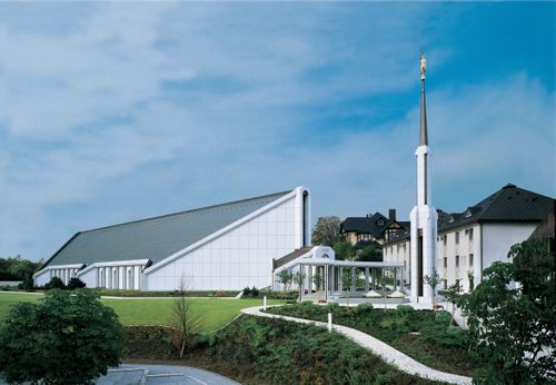 A view of the Frankfurt Germany Temple and its spire on a sunny day, with a blue sky above and green lawns in the front.