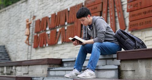 Young man reading a book while seated on steps outdoors.