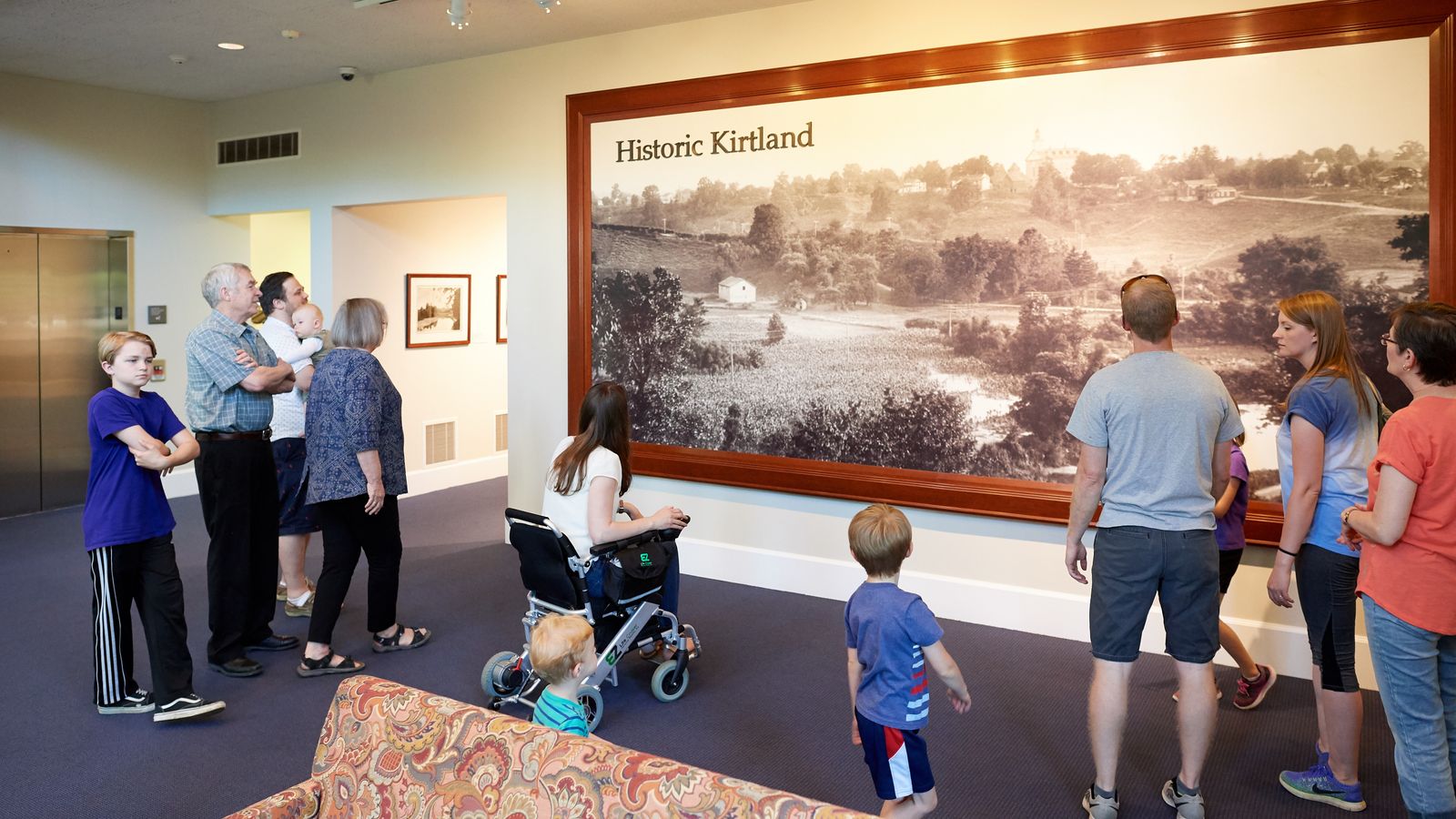 A group of people look at a large black and white photo on a wall depicting a landscape that has the words Historic Kirtland in the top left-hand corner.