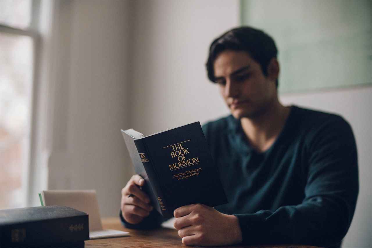 A man reading the Book of Mormon at his table