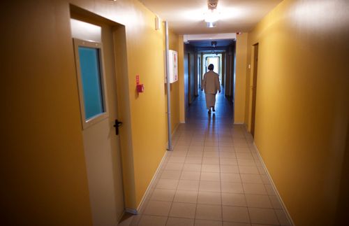 An elderly woman walking down the hall of a meetinghouse.