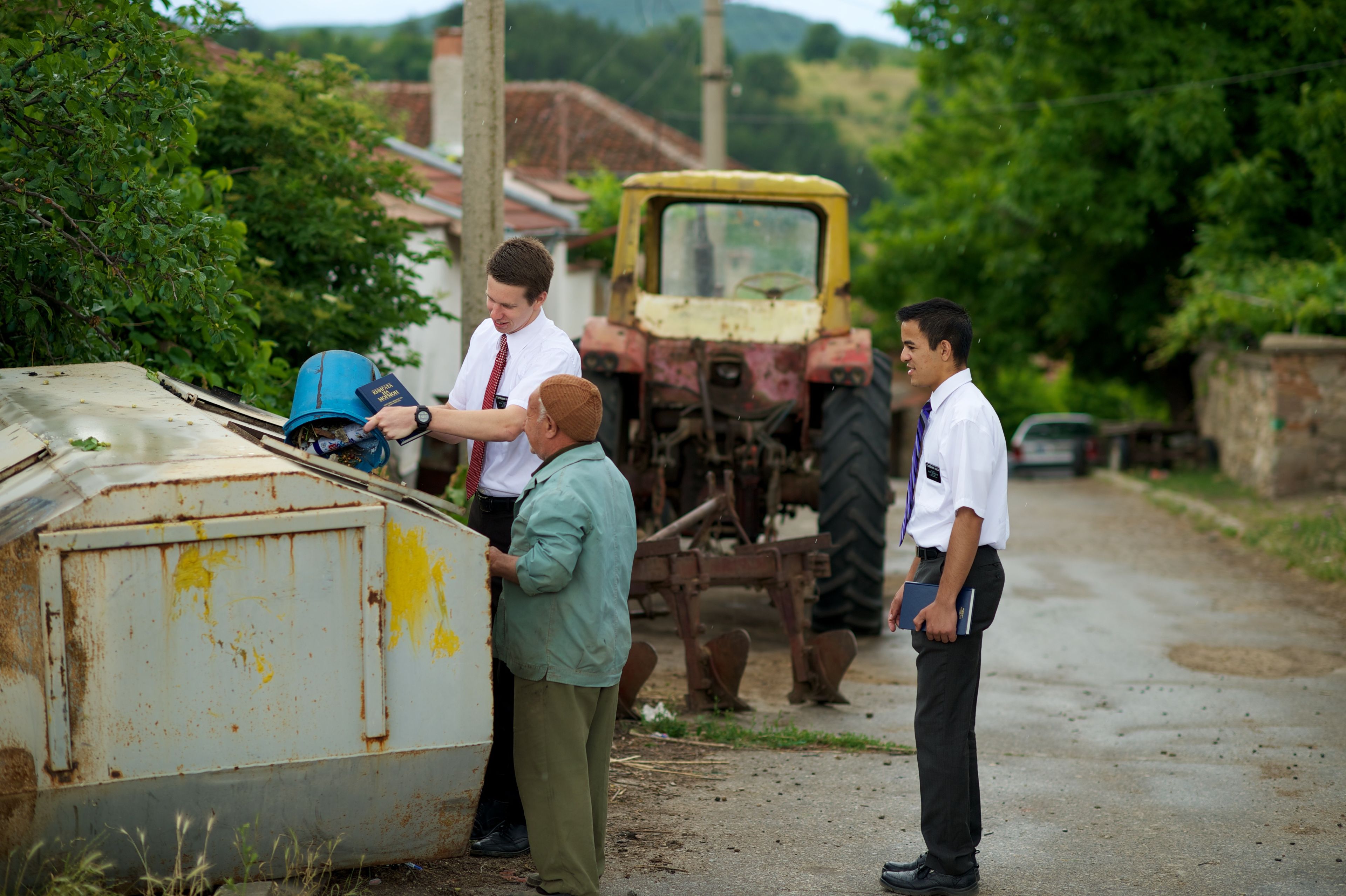 Two missionaries help an elderly woman take her trash to the dumpster down the street.