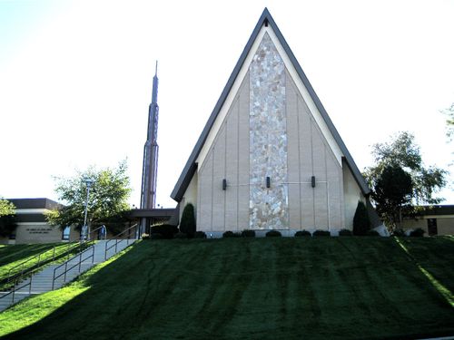A front view of a chapel in Bountiful, Utah, in an A-shape with a steeple in the back and a green, grassy hill leading up to the chapel.