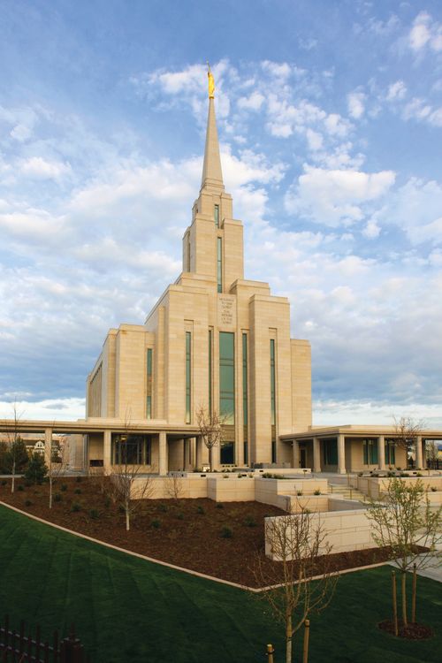 A front side view of the Oquirrh Mountain Utah Temple on a sunny day, with small trees growing on the grounds.