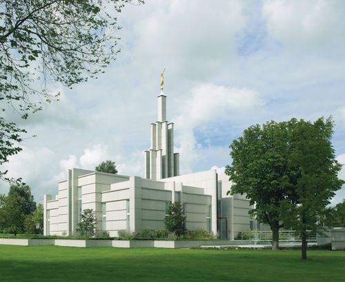 A view of The Hague Netherlands Temple from beyond green lawns, with large white clouds overhead.