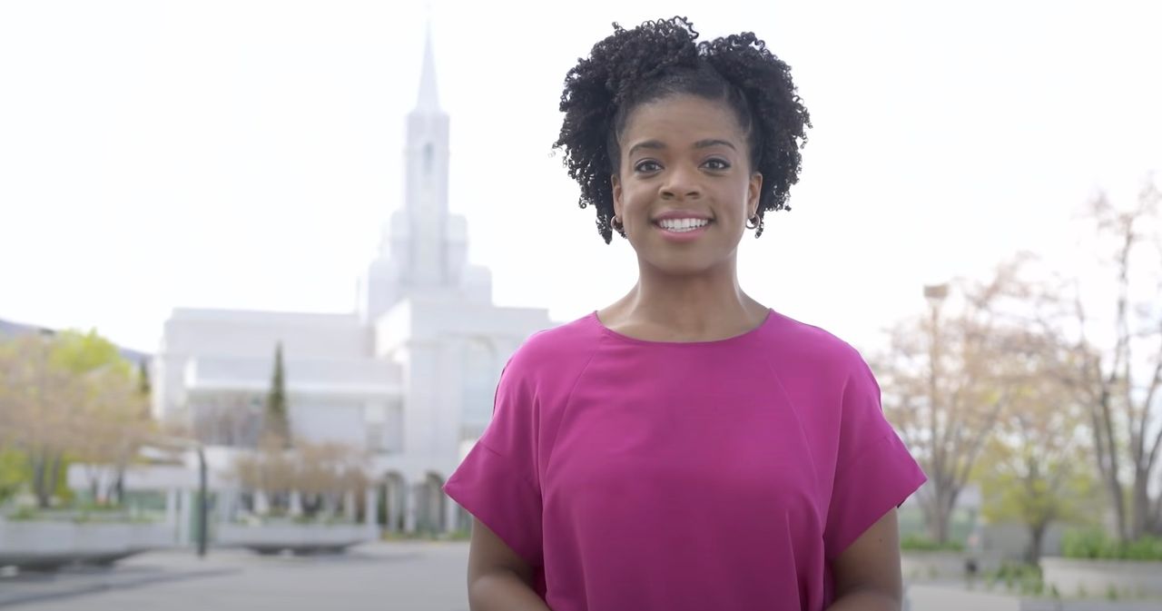 Una mujer de pie sonriendo frente al templo durante la primavera, para explicar por qué los bautismos por los muertos se efectúan en los templos