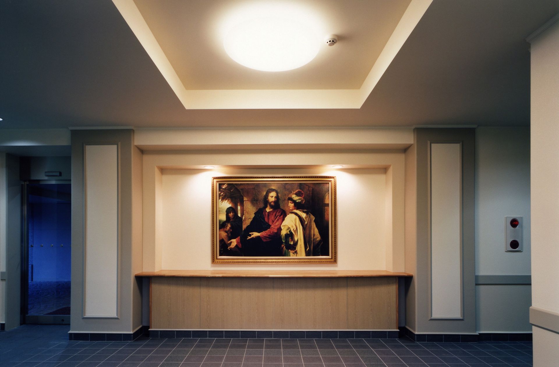 A meetinghouse foyer with a light shining on a painting of Christ.