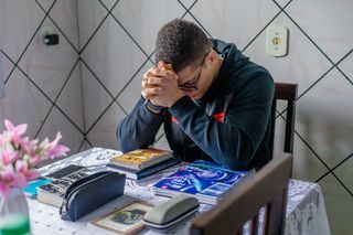 A young man folds his arms and prays in his home in Brazil. 