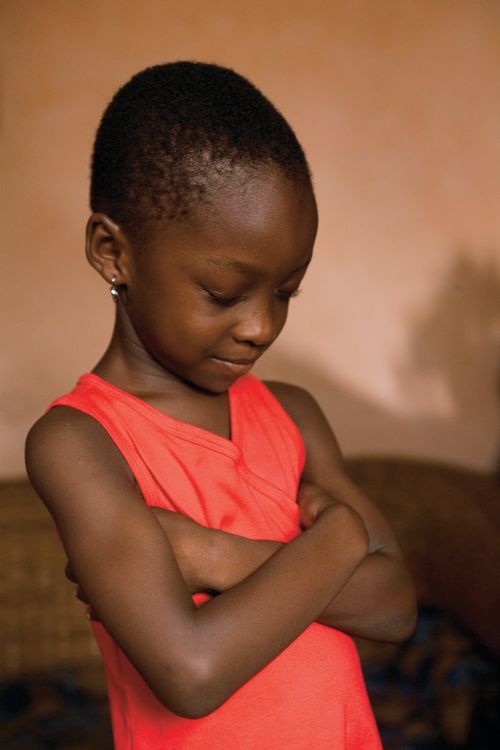 A young girl folds her arms, bows her head, and prays in her home in Ghana.