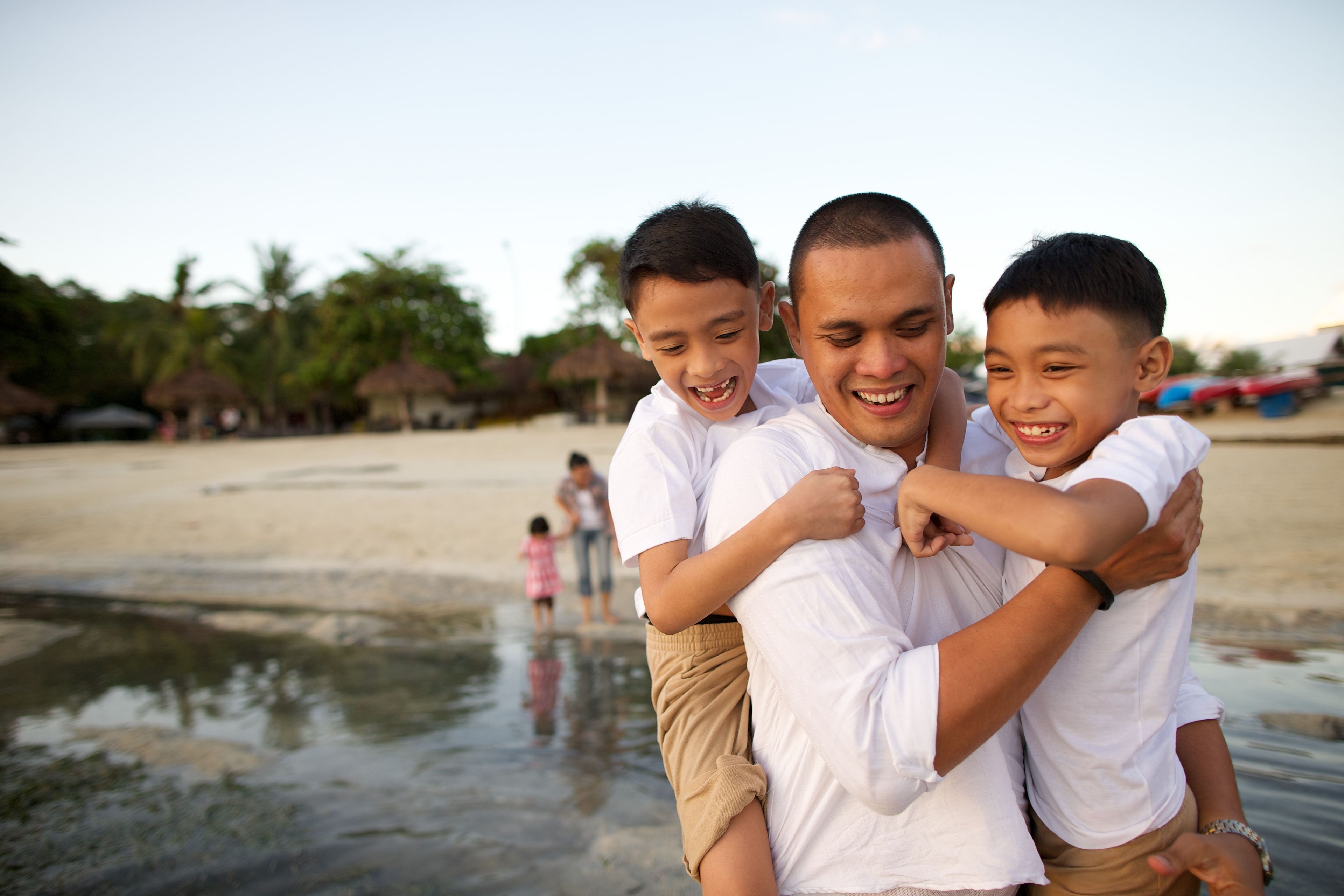 A father and his two sons run into the water at the beach.