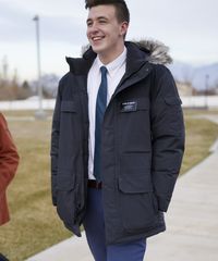 A missionary models appropriate shirts and ties. He is wearing a sweater while walking outside and carrying a bag.