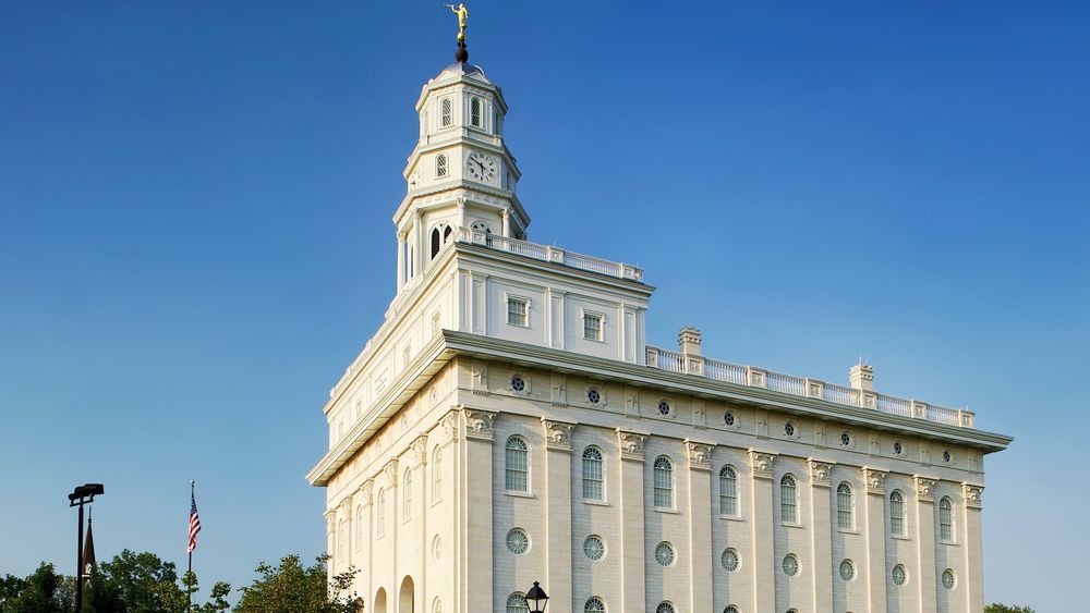 The side view of a large white building with a steeple. A grassy lawn surrounds it.