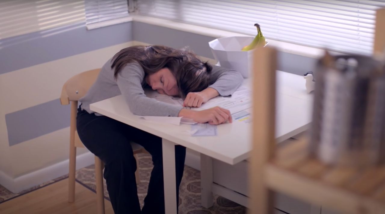 An exhausted woman rests her head on her kitchen table