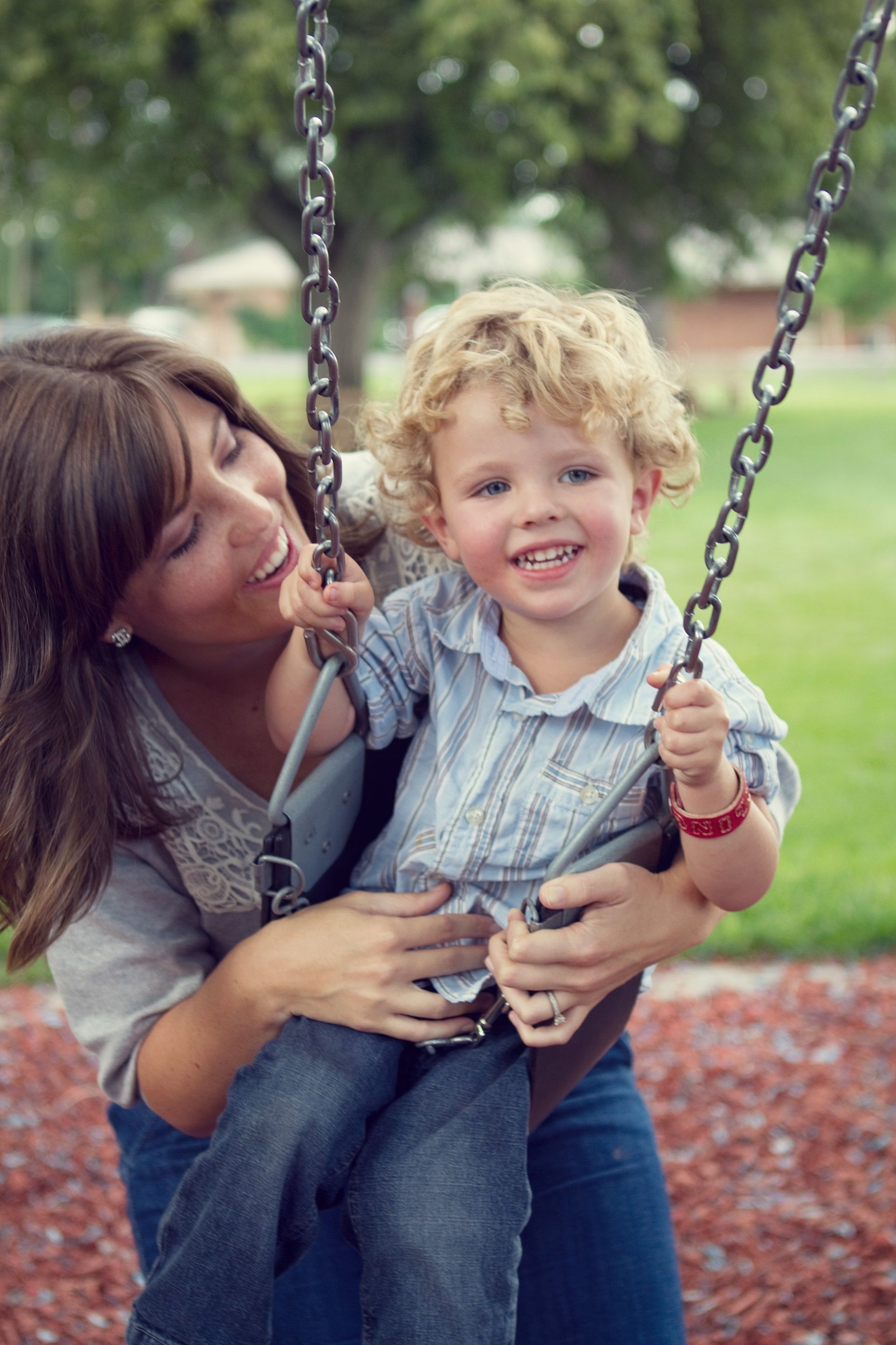 A mother pushes her son on the swing.