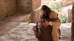 Hombre sanado a los pies de Jesús abrazándose