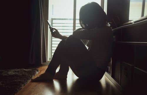 a woman sitting in the dark and scrolling on her phone