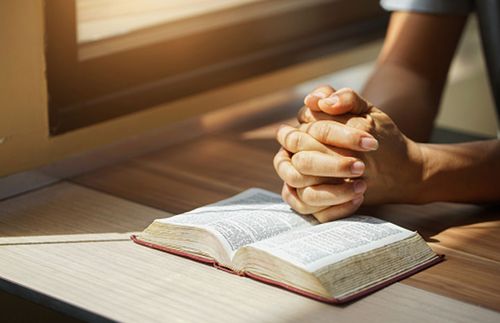 hands clasped in prayer over a set of scriptures