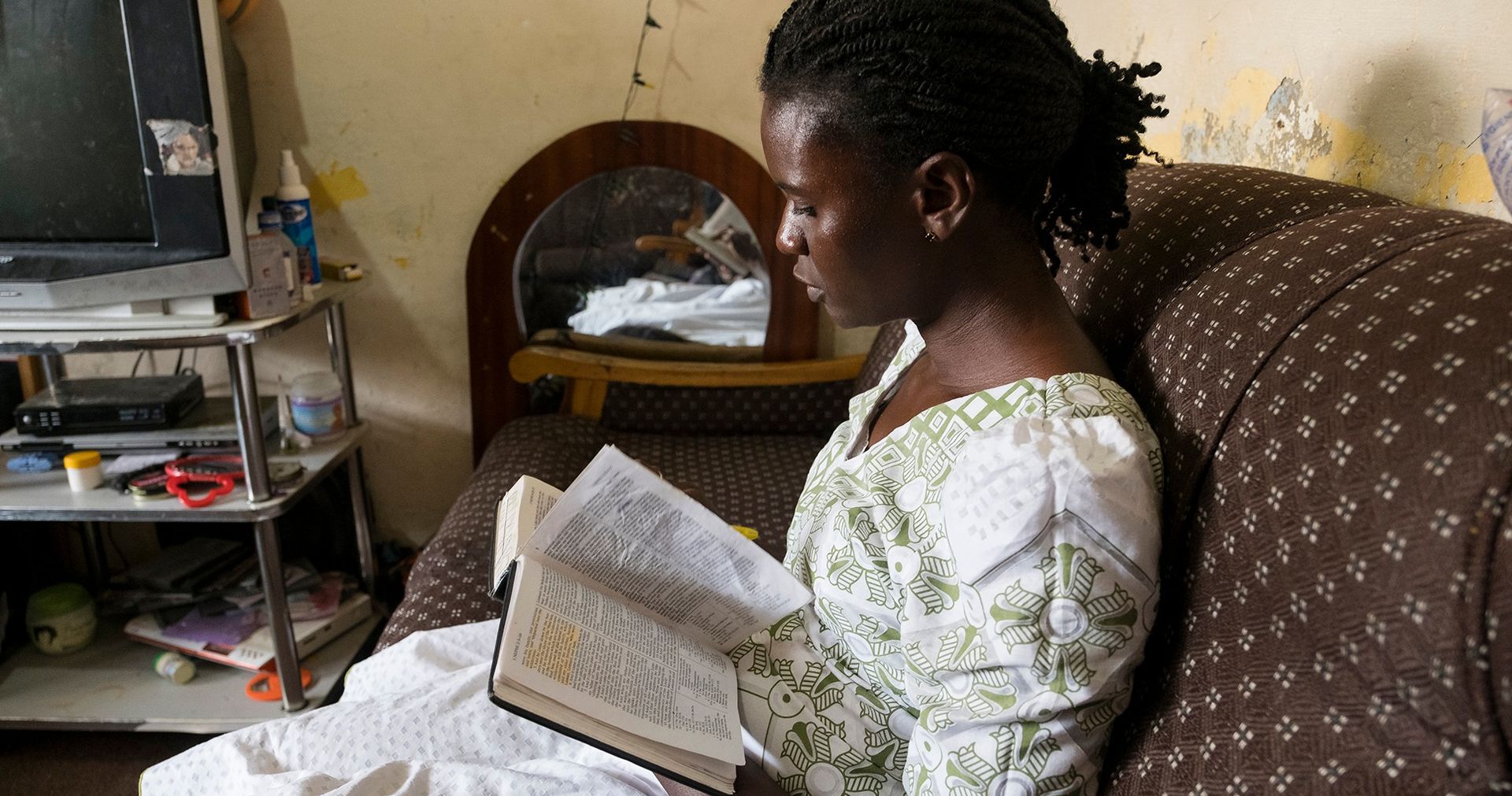 A Ghanaian woman sits on her couch reading the scriptures.