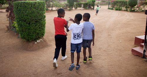 Three boys walk together in South Africa in a garden-like area.