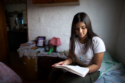 A young dark-haired woman in Uruguay sitting on her bed and studying the scriptures.