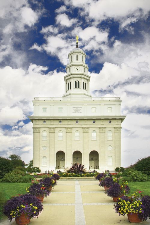 A portrait view of the front of the Nauvoo Illinois Temple, with a flower-lined path leading toward the temple’s entrance.
