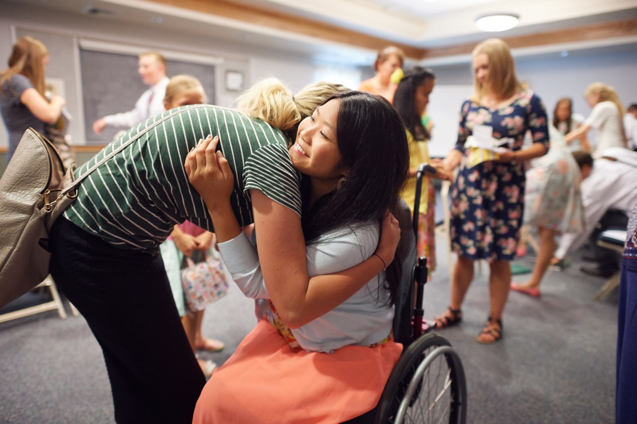 A young woman in a wheel chair is greeted by a friend at the end of a church meeting
