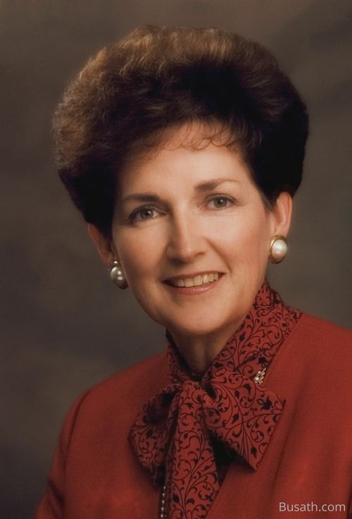A photograph of Janette Callister Hales Beckham against a brown background, wearing a red blazer and blouse.