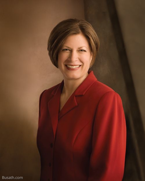 A photograph of Julie Bangerter Beck against a brown background, wearing a red blazer.