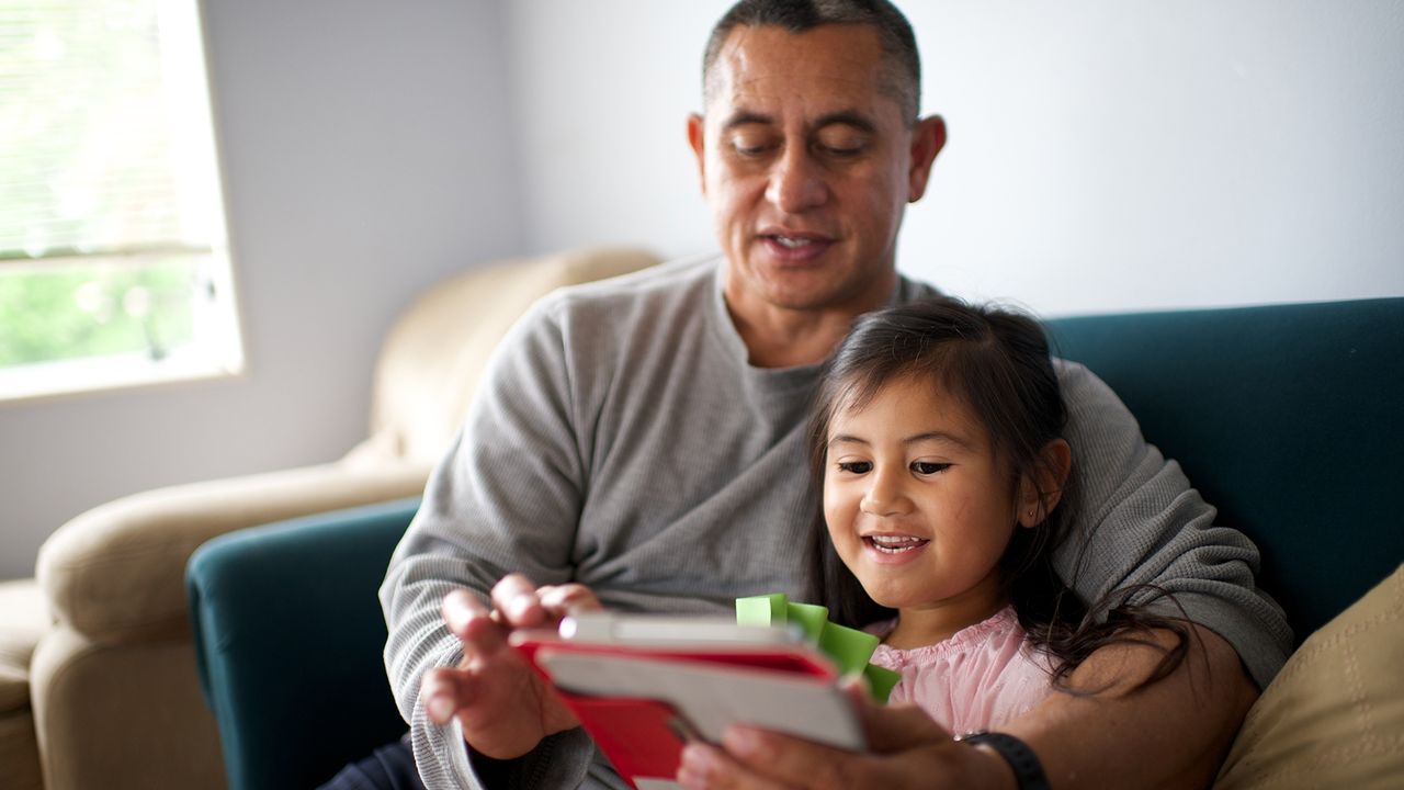 Uma menina e seu pai leem a Bíblia Sagrada em um tablet