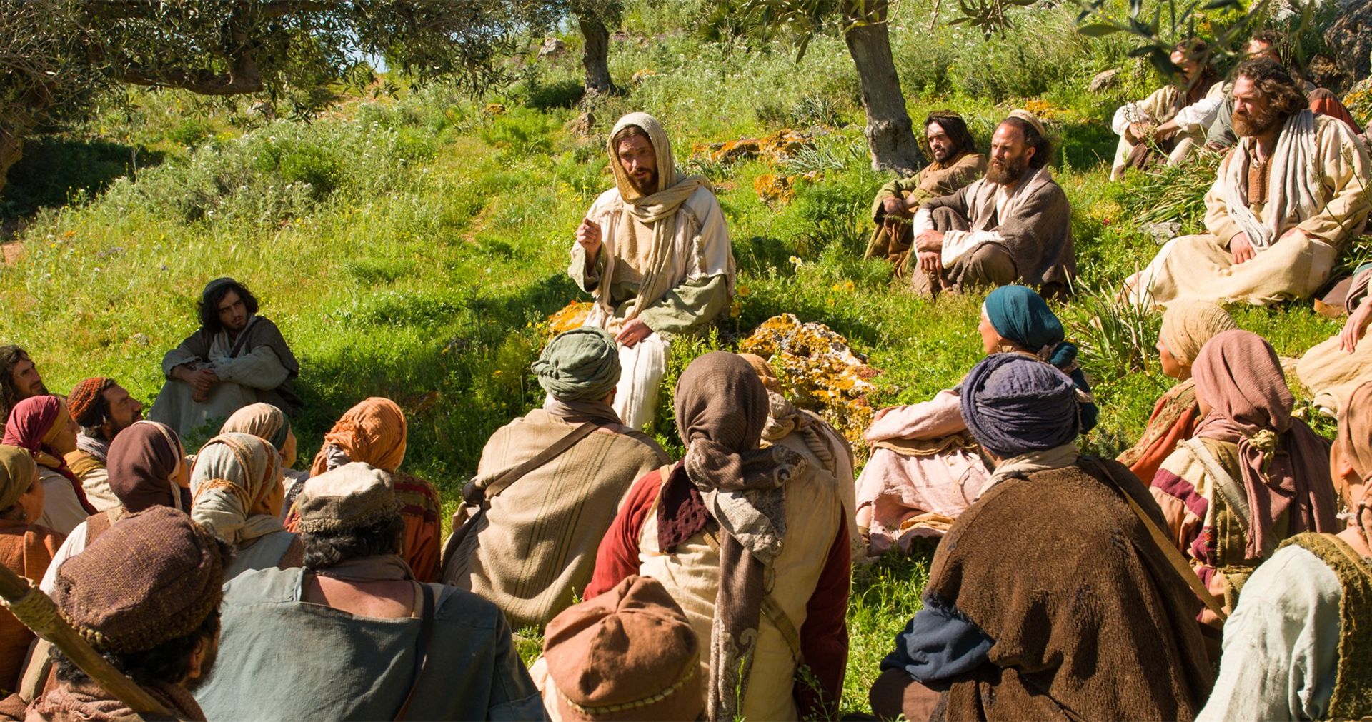 Jesus teaching a small group of people sitting on a green hill.