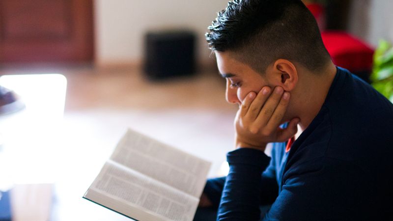 Un hombre joven estudia el Libro de Mormón desde la sala de su casa