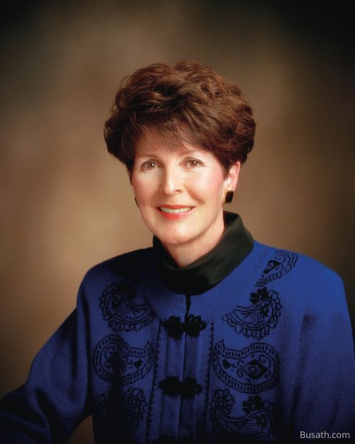 A photograph of Patricia Peterson Pinegar seated against a brown background, wearing a blue blouse with a black collar.