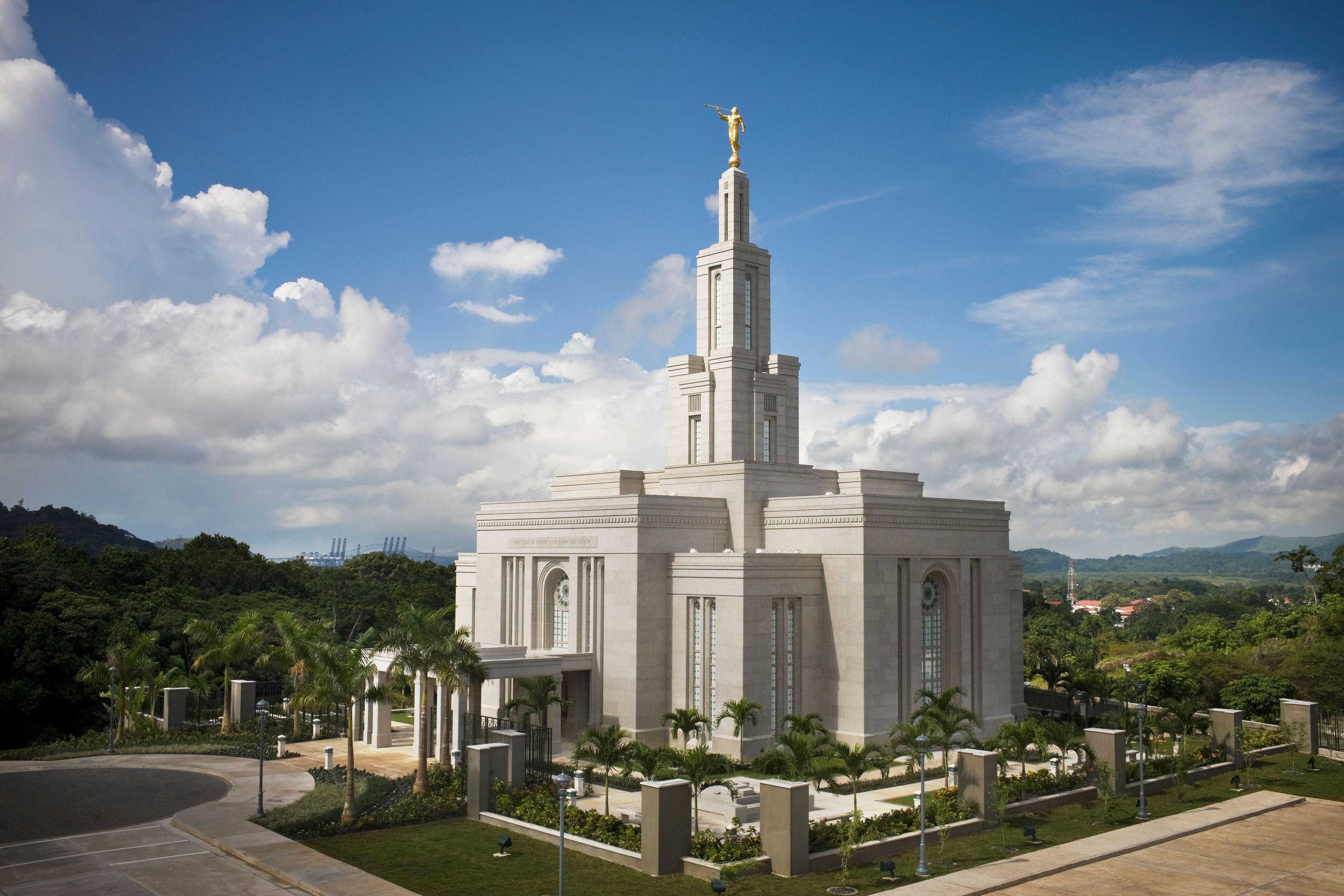 A side view of the Panama City Panama Temple, surrounded by palm trees, with large white clouds overhead.