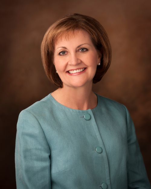 A portrait of Sister Linda K. Burton, who is wearing a turquoise jacket, in front of a brown background.