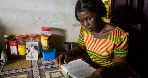 Woman reads scriptures at a table in her home in Sierra Leone.