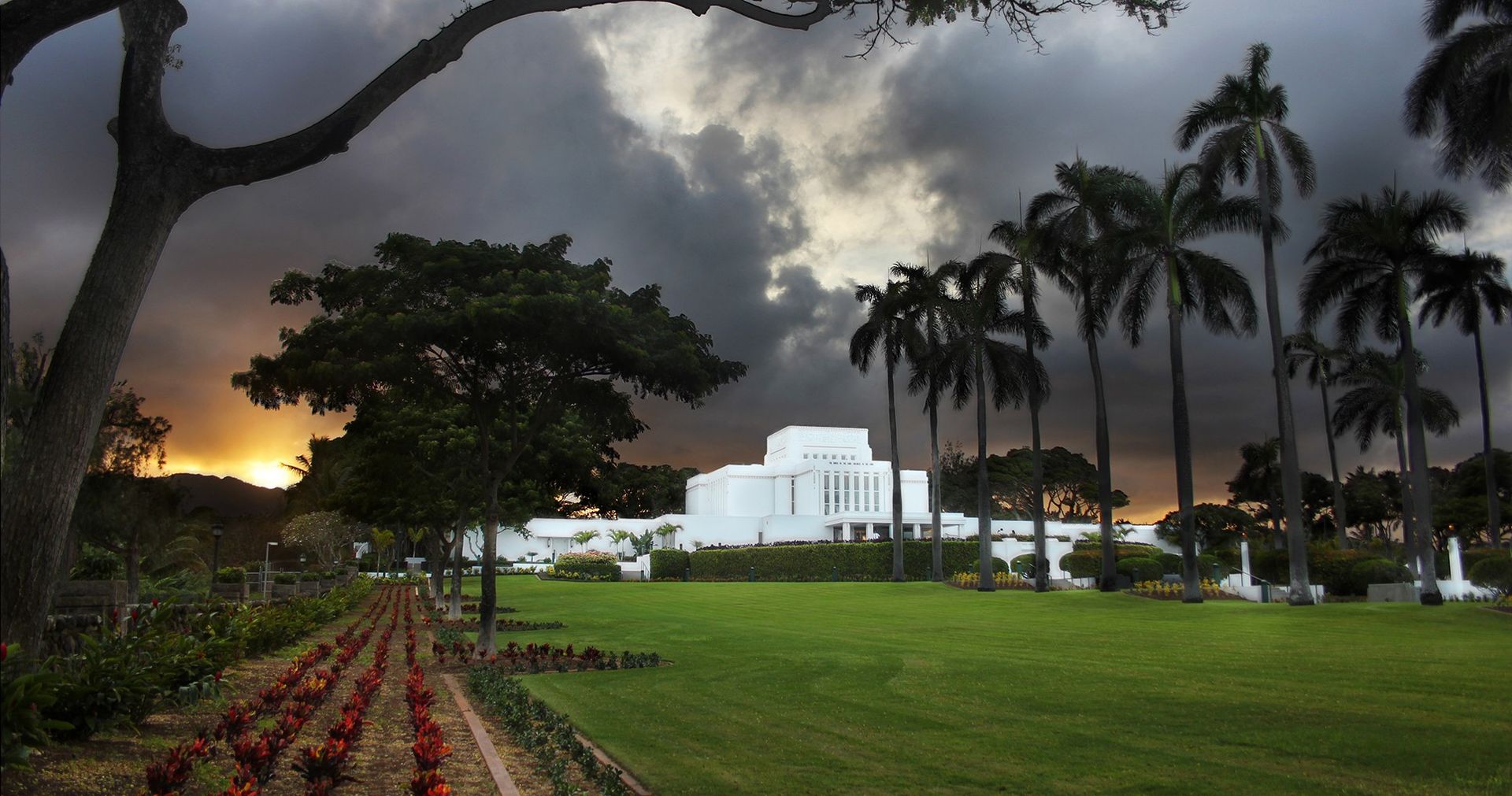 Exterior photo of the Laie Hawaii Temple with dark clouds in the background.