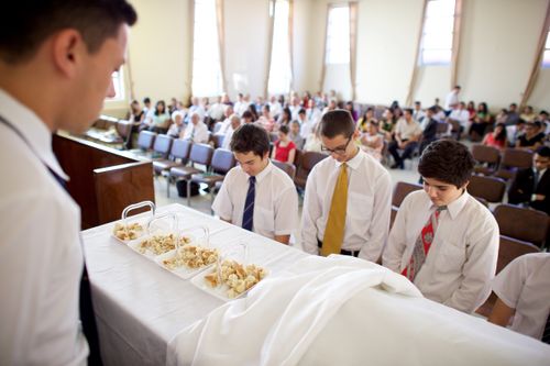 Young men in Paraguay stand around the sacrament table with their heads bowed.