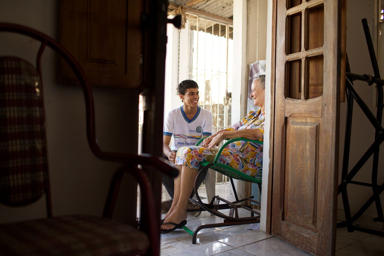 A young man sits on a porch with an older woman as they visit and enjoy the gospel of Jesus Christ