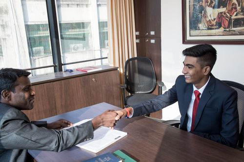A prospective missionary sits at a desk, shaking hands with his district president in Mumbai, India, following an interview.