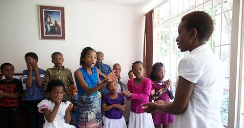 A Primary leader conducting music as children stand to sing.