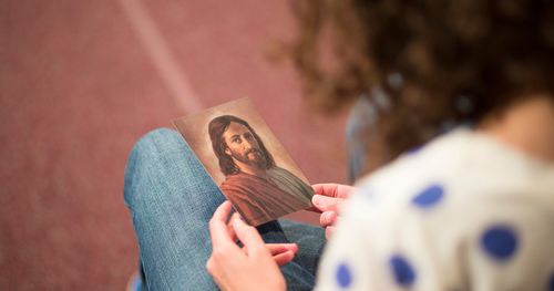 Mulher olha uma pequena gravura de Jesus Cristo. A imagem é reprodução de uma pintura de Robert Barrett.