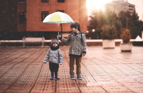 pieni poika pitelee sateenvarjoa toisen lapsen yllä