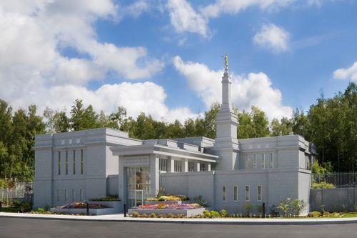 The Anchorage Alaska Temple on a sunny day, with flowers in the front and green trees in the background.